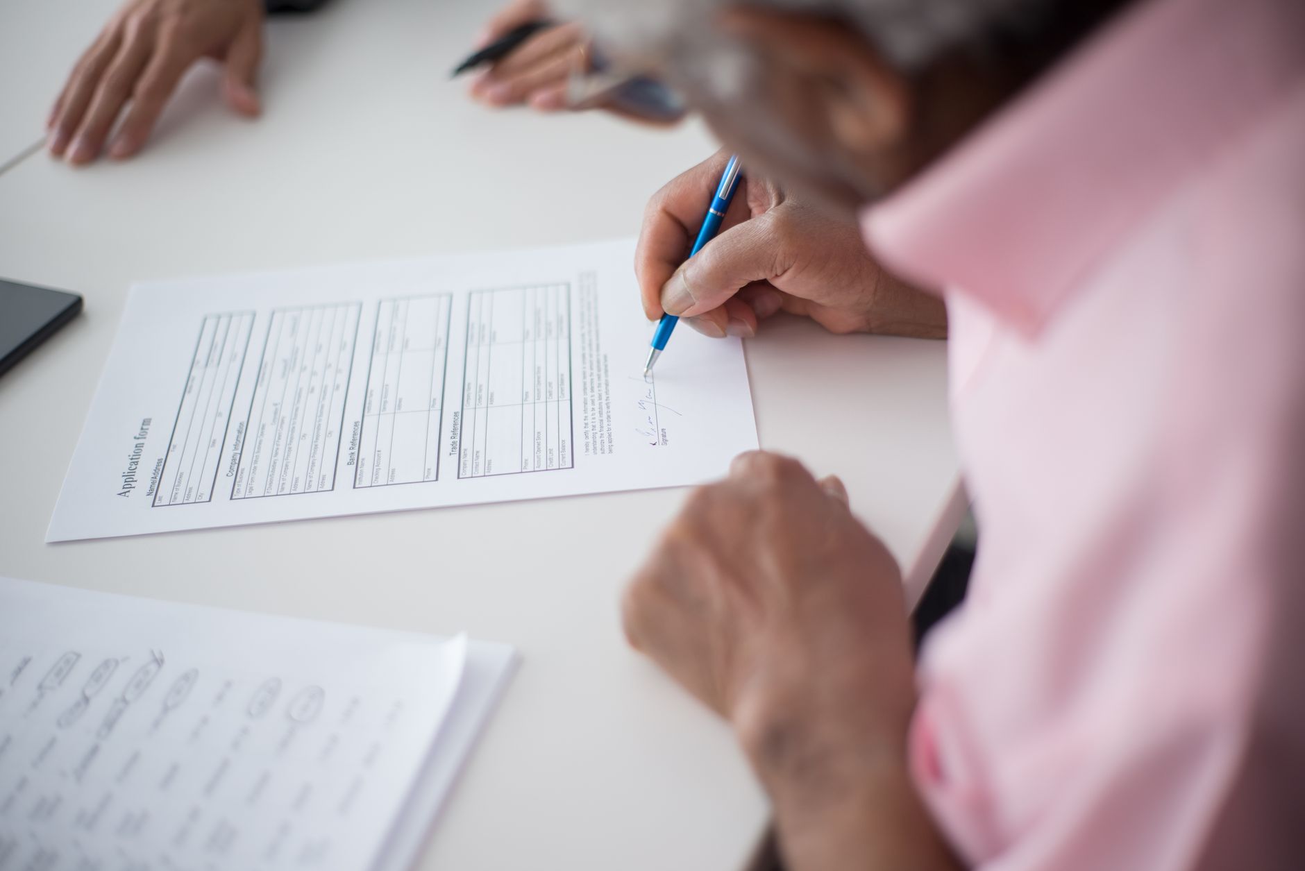Hands signing an application form with a pen