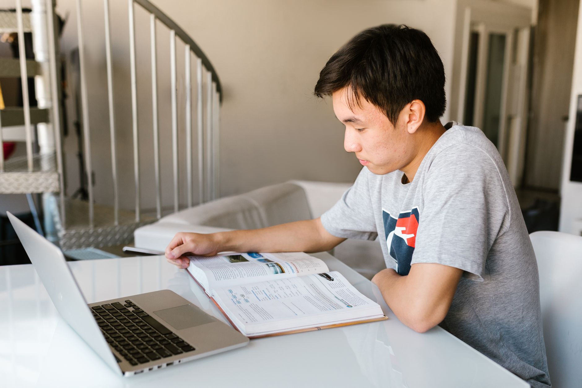 Student studying with a laptop and textbook near a bright window